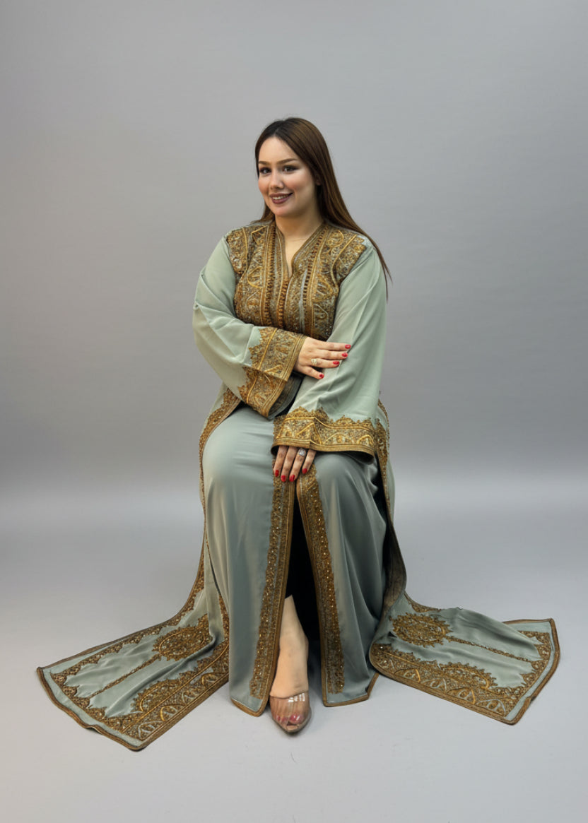 A woman wearing a sage green traditional moroccan kaftan outfit with gold embroidery.