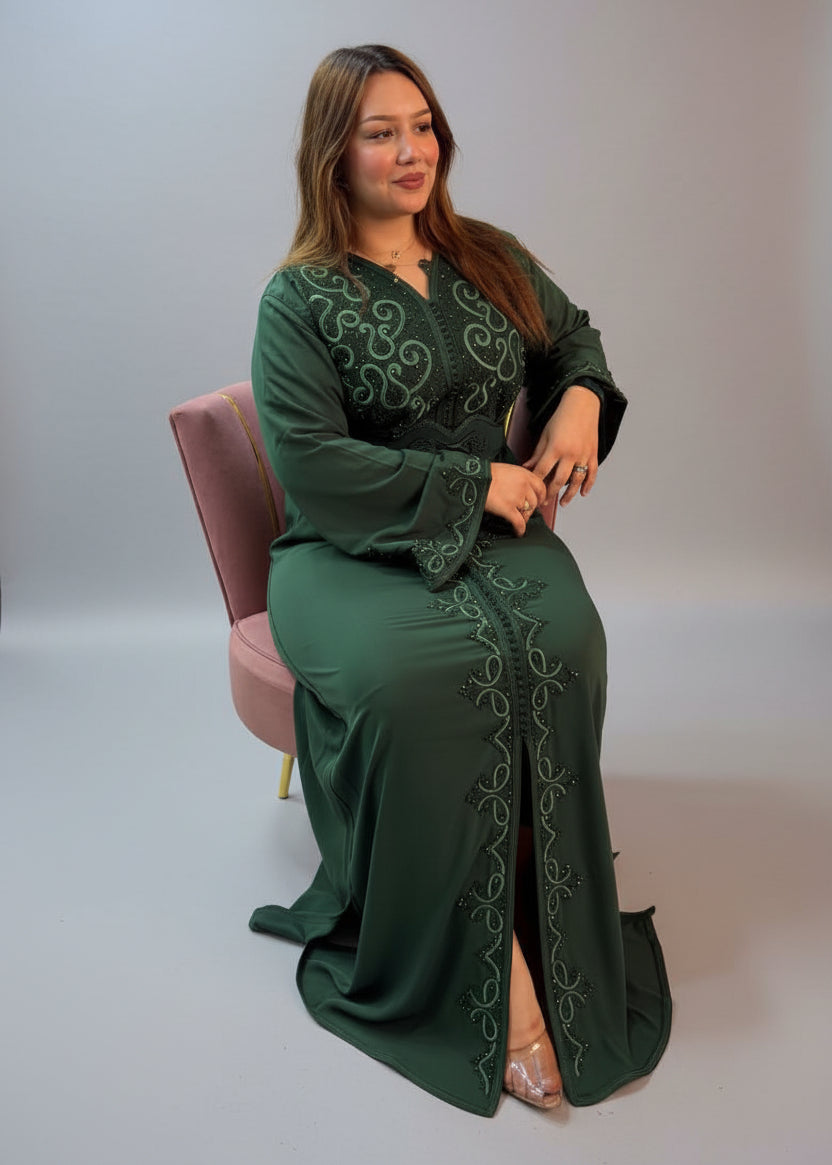 A woman wearing a dark green long-sleeved maxi kaftan with intricate embroidery, seated in a chair.