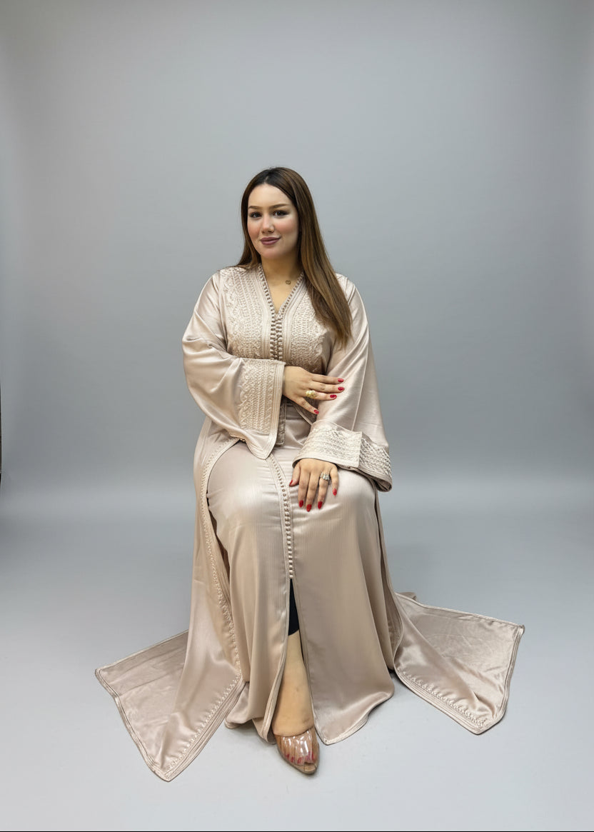 A woman wearing a beige satin kaftan and matching jacket sits.