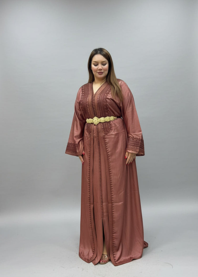 A woman modeling a long, floor-length dusty rose kaftan with a gold belt.