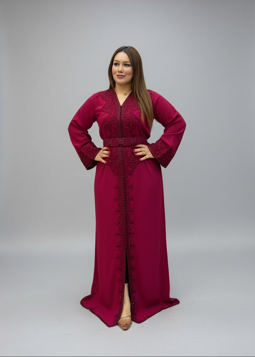 A woman modeling a long magenta maxi caftan with lace sleeves and a matching belt .