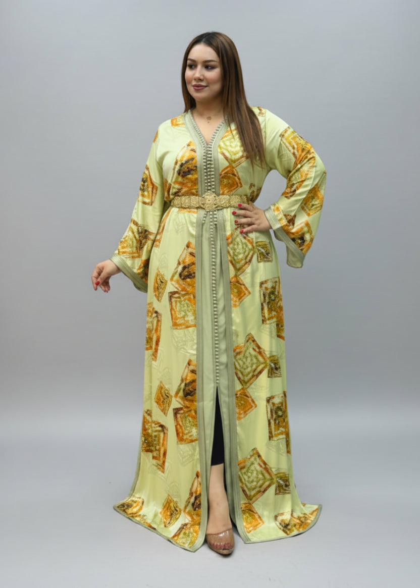 A woman modeling a long, light green kaftan dress with yellow and orange geometric patterns.
