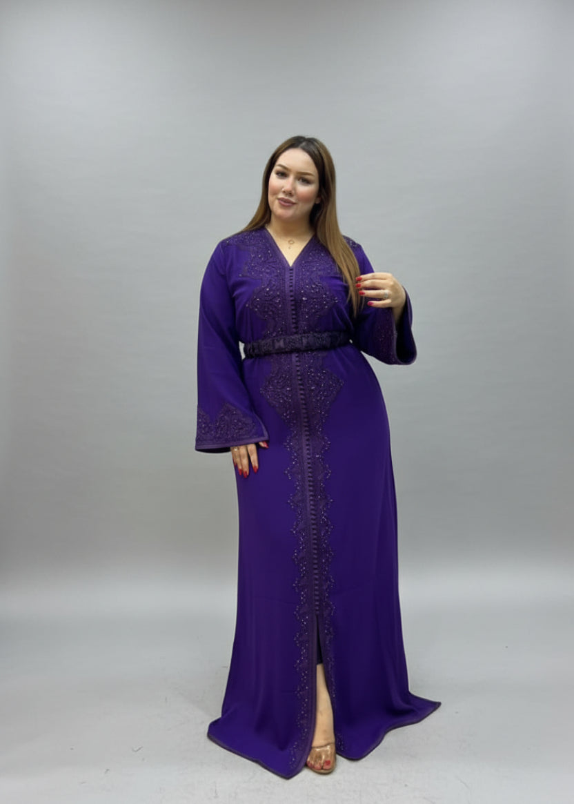 A woman modeling a long purple embroidered caftan with a black belt.