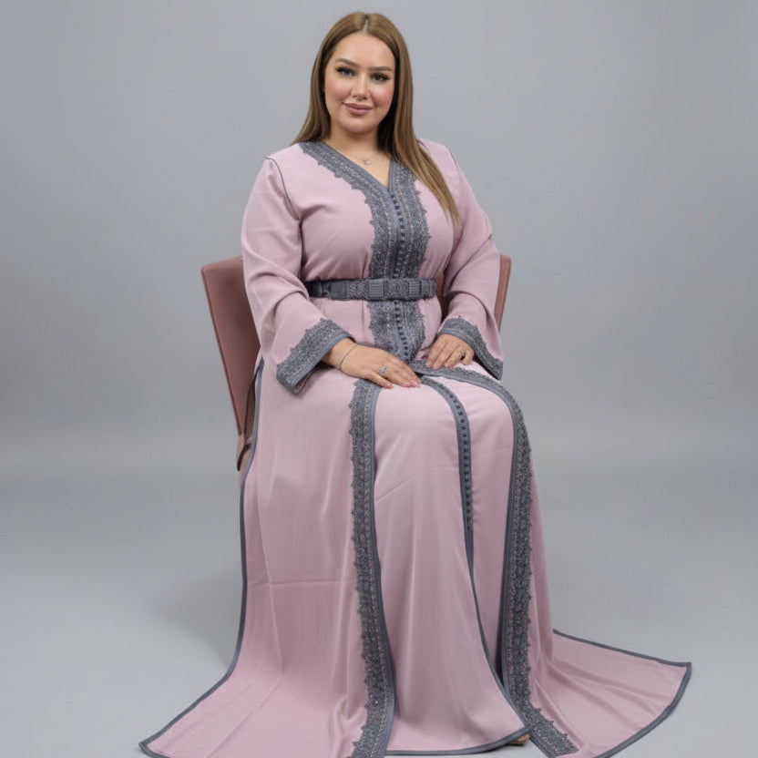 Elegant woman wearing a pink caftan with gray accents, seated in a chair against a neutral background.