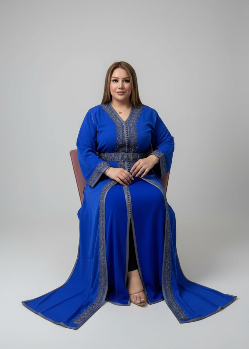 Model wearing a blue caftan with intricate details, sitting gracefully in a studio setting.