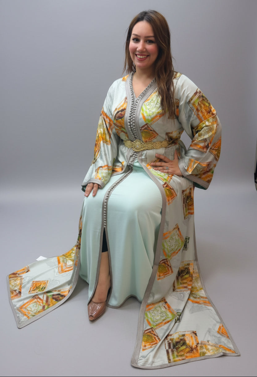 A woman wearing a traditional Moroccan caftan (Dress of the Sultan) in a mint green color with orange and gold geometric patterns.