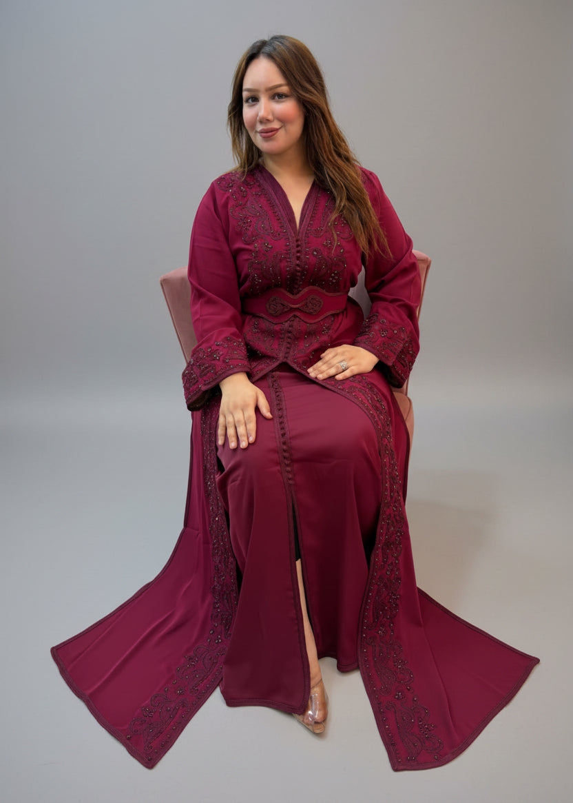 A woman wearing a long maroon kaftan with intricate embroidery and a matching headscarf.