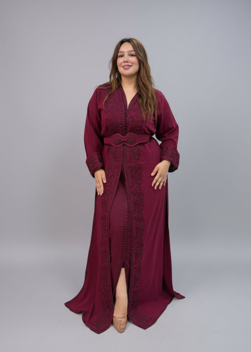 A woman modeling a long burgundy maxi kaftan with matching embroidered sleeves and a waist tie.