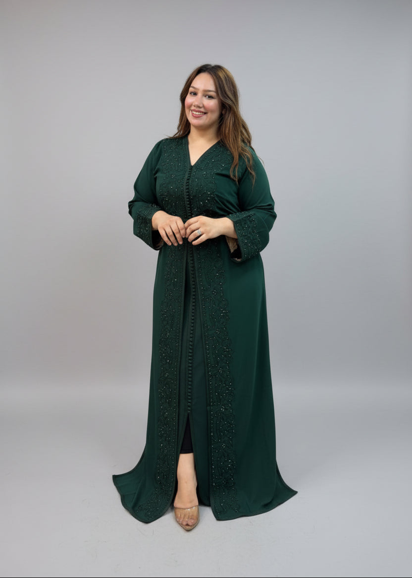 A woman modeling a dark green embroidered Caftan with a matching inner black dress.