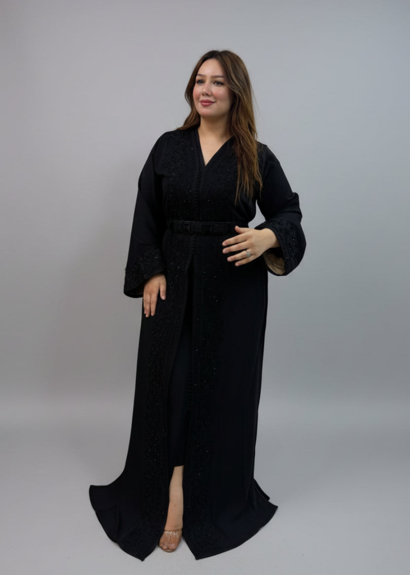 A woman modeling a long black embroidered kaftan with a matching belt.