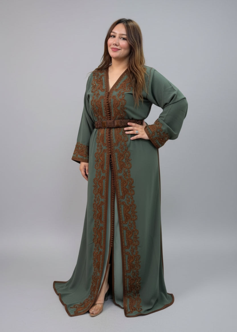 A woman modeling a long sage green kaftan dress with brown floral embroidery and a matching brown bel.