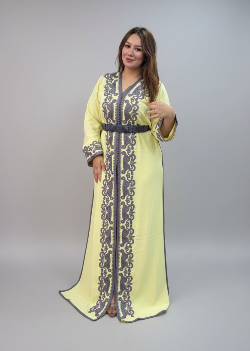 A woman modeling a pale yellow kaftan dress with dark gray embroidery.