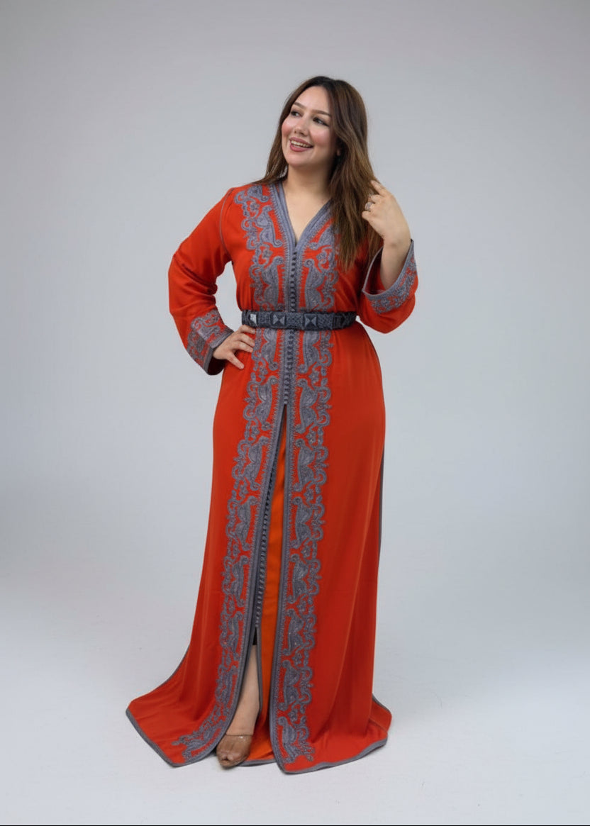 A woman modeling a long orange-red caftan with gray embroidery and a gray belt.