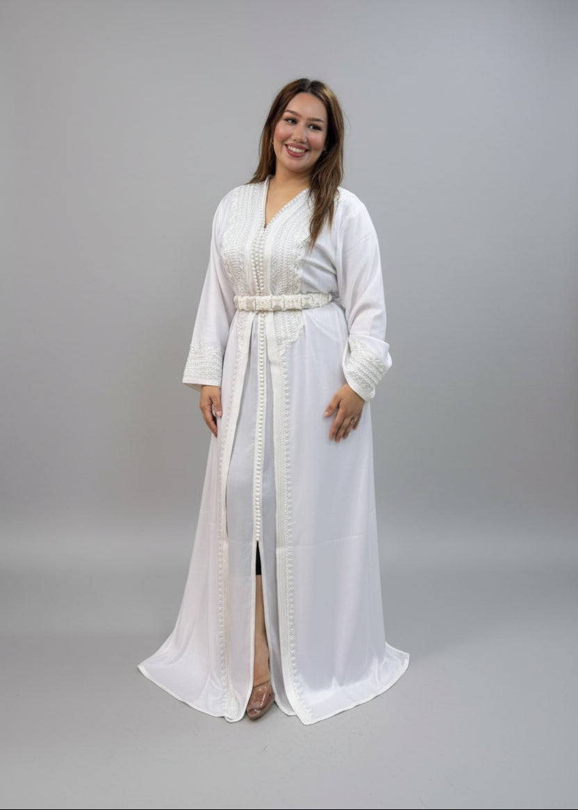 A woman wearing a white long-sleeved embroidered kaftan stands .