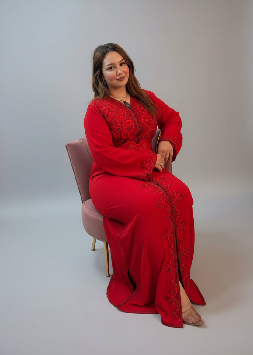 A woman wearing a long-sleeved red maxi kaftan with intricate black embroidery sits i
