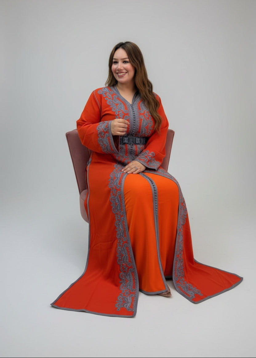 A woman wearing a bright orange traditional long Caftan with gray embroidered borders sits in a chair.