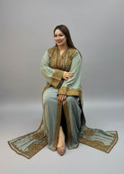 A woman wearing a sage green traditional moroccan kaftan  outfit with gold embroidery.