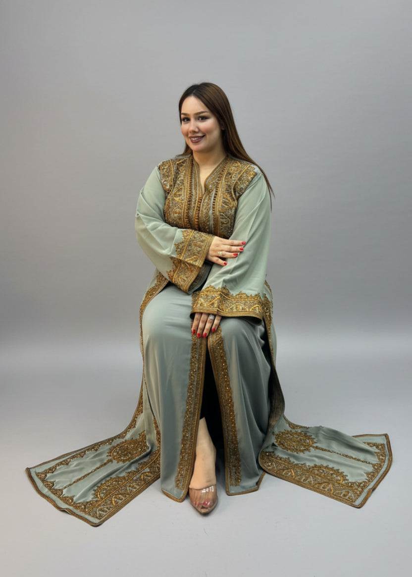 A woman wearing a sage green traditional moroccan kaftan  outfit with gold embroidery.