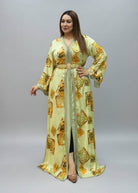 A woman modeling a long, light green kaftan dress with yellow and orange geometric patterns.