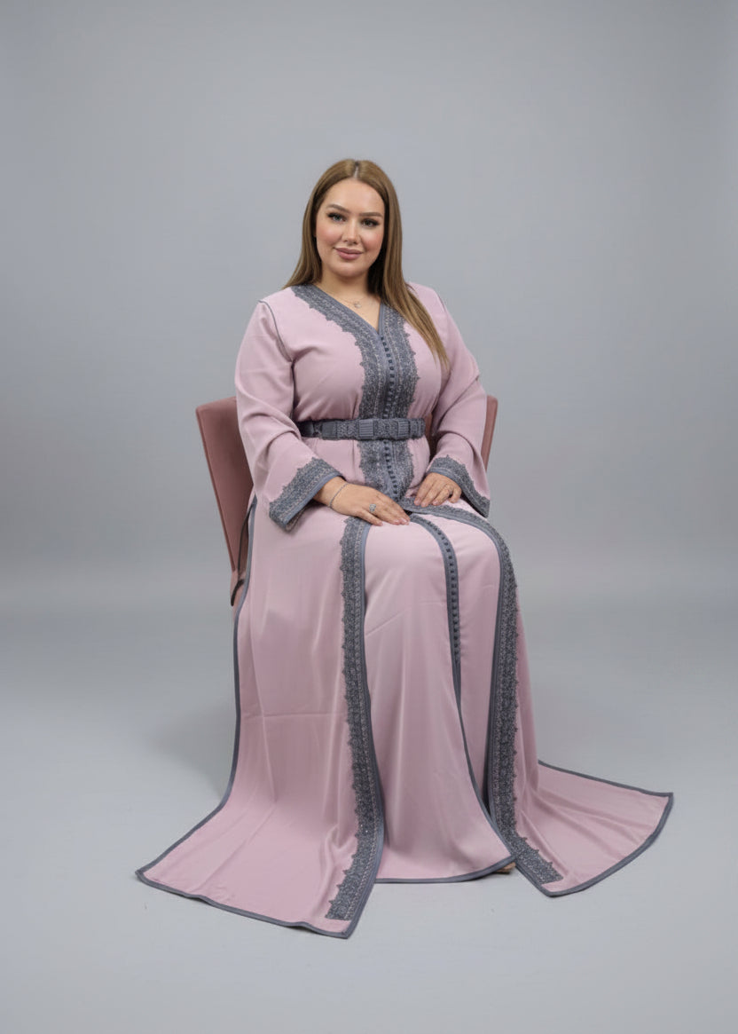 Elegant woman wearing a pink caftan with gray accents, seated in a chair against a neutral background.