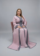 Elegant woman wearing a pink caftan with gray accents, seated in a chair against a neutral background.