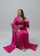 A woman wearing a bright magenta pink traditional caftan with gold embroidery and a gold belt, 