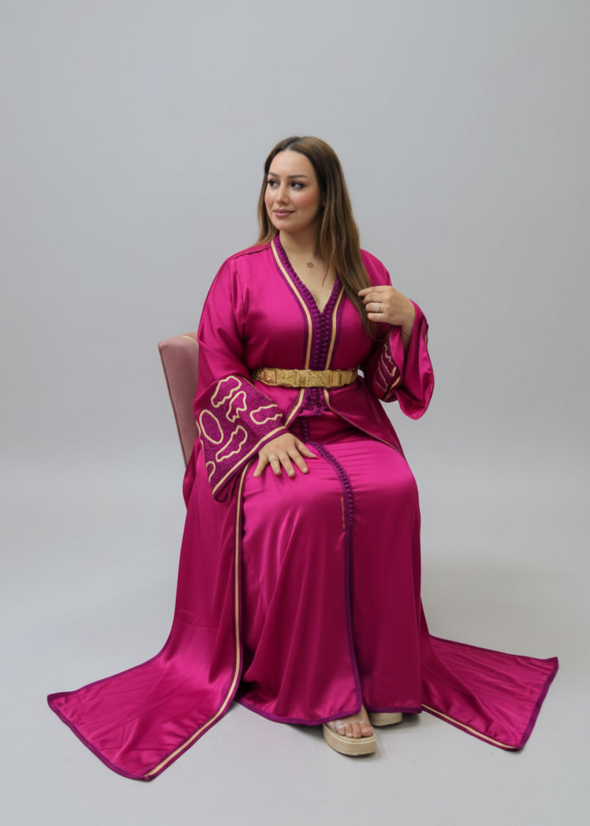 A woman wearing a bright magenta pink traditional caftan with gold embroidery and a gold belt, 