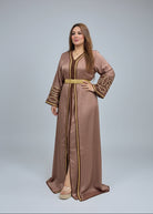 A woman modeling a traditional long brown caftan dress with gold embroidery and a gold belt