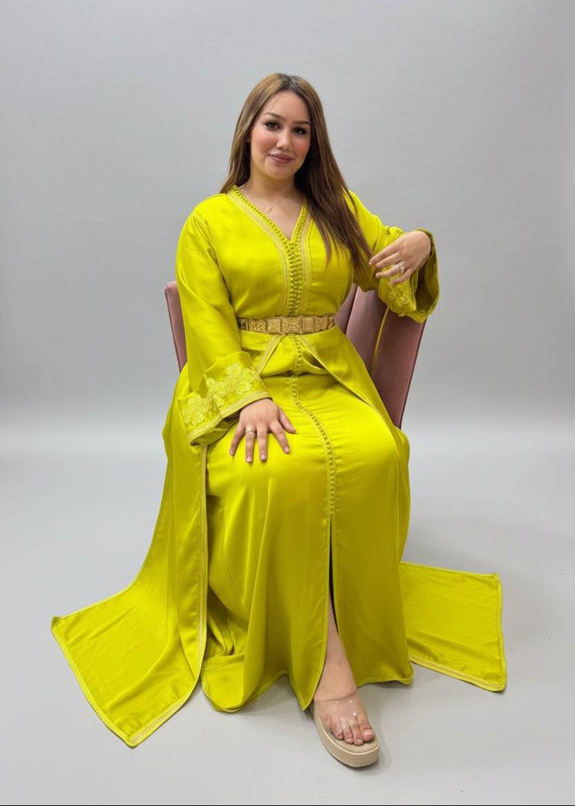 A woman wearing a bright yellow traditional long Caftan with a matching belt sits in a kaftan store.