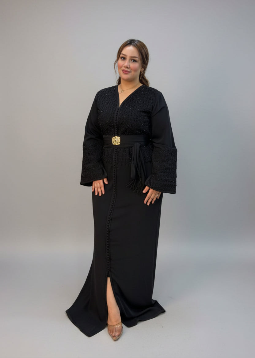 A woman modeling a black long kaftan dress with a gold belt 