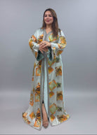 A woman modeling a long, light sage green kaftan dress with orange and yellow geometric patterns.