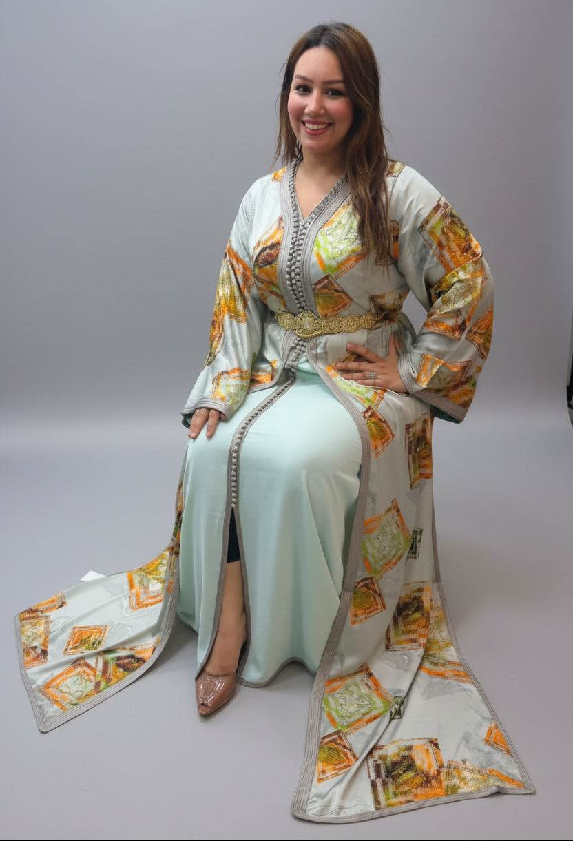 A woman wearing a traditional Moroccan caftan (Dress of the Sultan) in a mint green color with orange and gold geometric patterns.