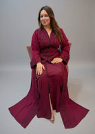 A woman wearing a long maroon kaftan with intricate embroidery and a matching headscarf.
