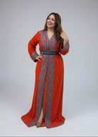 A woman modeling a long orange-red caftan with gray embroidery and a gray belt.