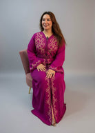 A woman wearing a bright magenta-purple traditional long Moroccan Kaftan with gold embroidery