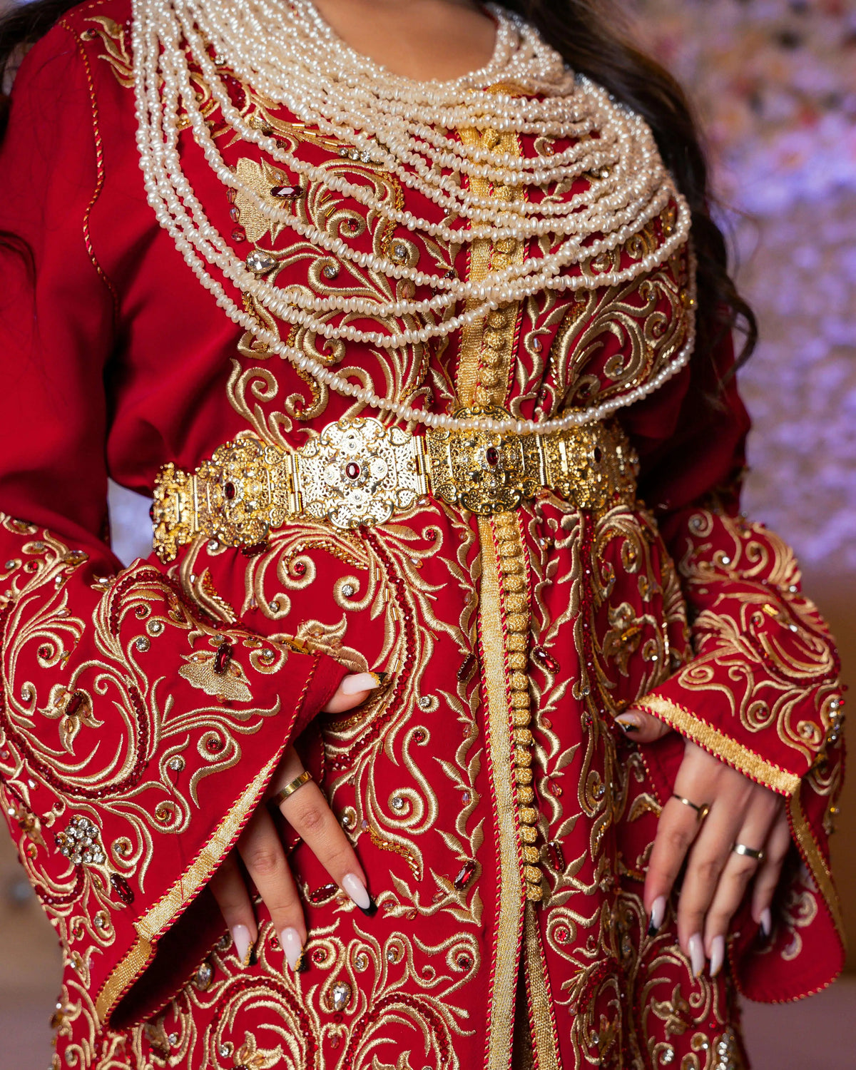 Woman wearing a luxury Moroccan caftan in red and gold with intricate embroidery, traditional belt and pearl jewelry — YourCaftan