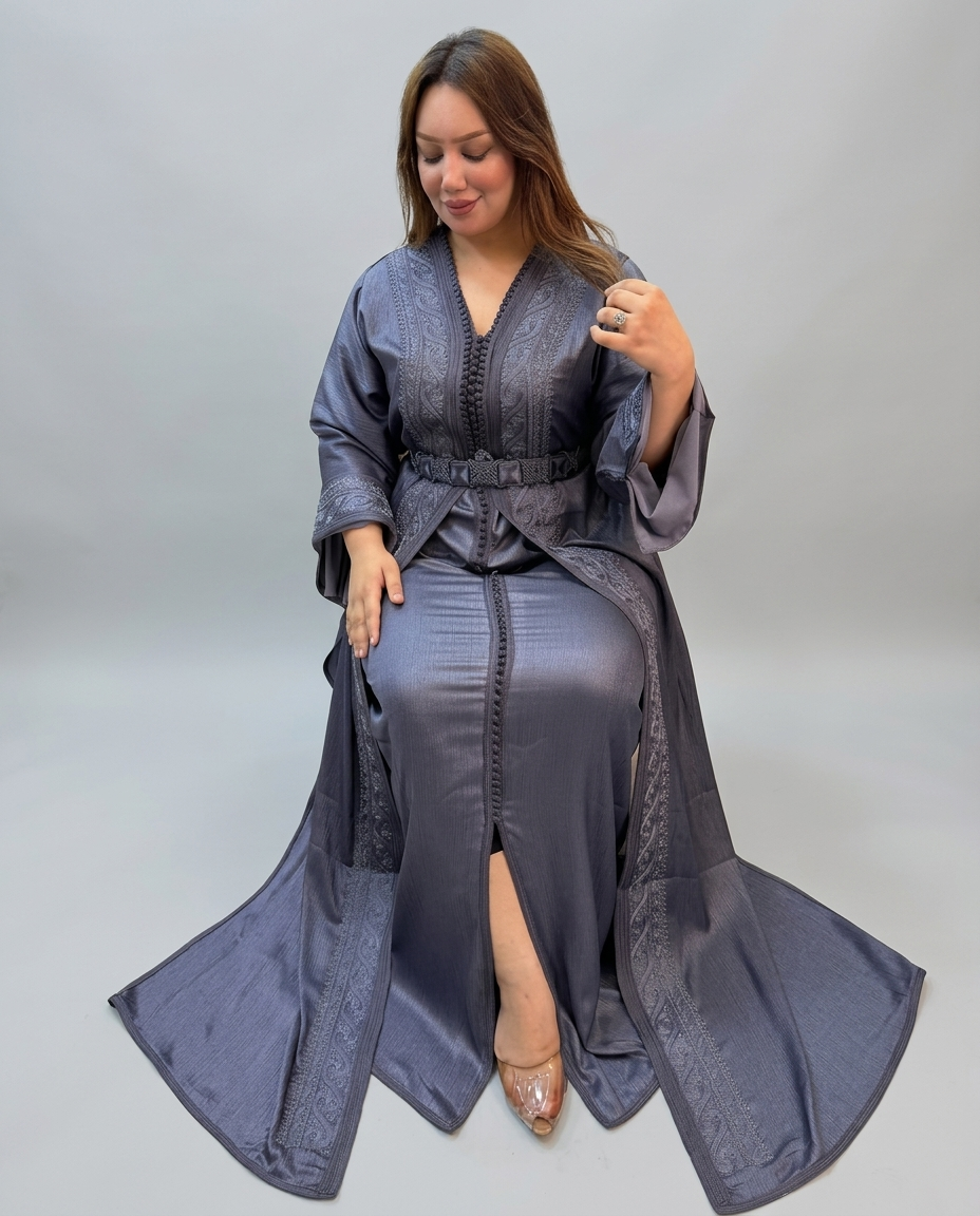 A woman wearing a long, floor-length gray kaftan with wide sleeves, a V-neck, and a matching waist tie, posed against a plain light gray studio background.