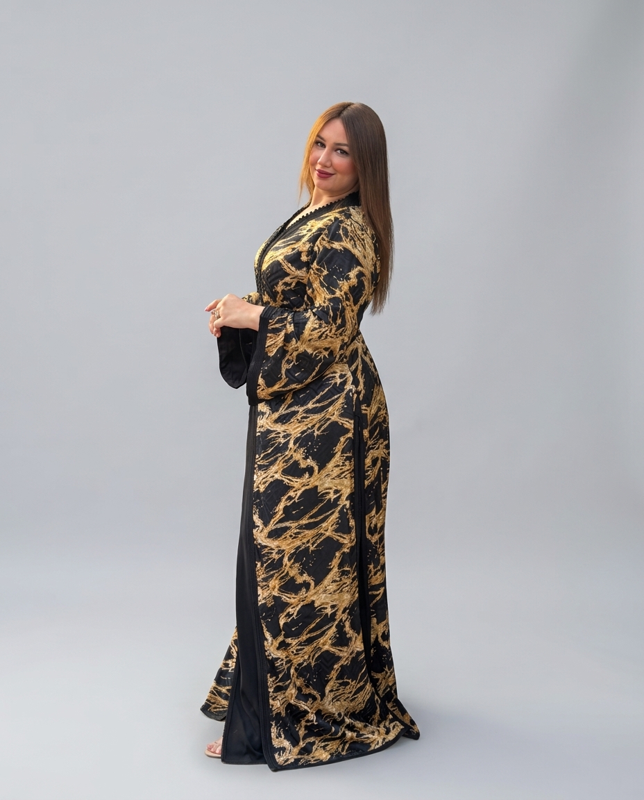 A woman modeling a long black and gold patterned robe with wide sleeves, standing against a plain light gray studio background.