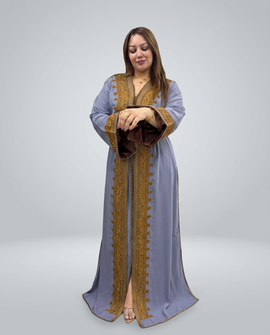A woman modeling a long, floor-length light blue abaya with ornate gold embroidery and trim, standing against a neutral gray studio background.